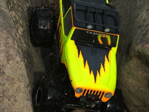 1996 Ford Bronco - This remote-controlled vehicle features bright yellow paint with flame graphics and a Tamiya logo, navigating a rocky terrain.
