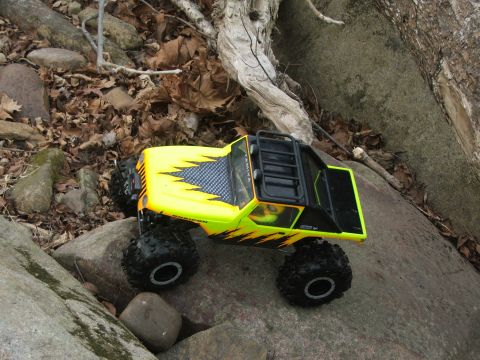 1996 Ford Bronco - A yellow remote control rock crawler with black flame decals navigates a rocky terrain.