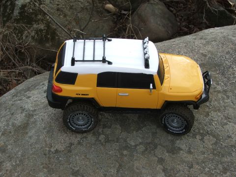 1996 Ford Bronco - A toy SUV with a white roof and rack sits on a large rock outdoors.