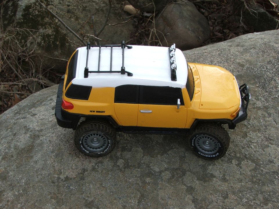 Yellow and white toy SUV with roof rack and light bar on a rock