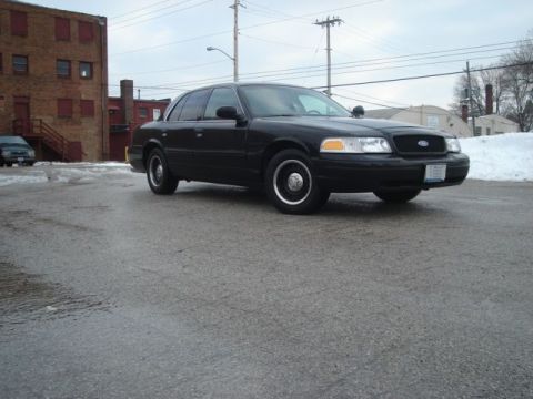 2000 Ford Crown Victoria - A black 2000 Ford Crown Victoria is parked on a wet asphalt lot with a brick building in the background.