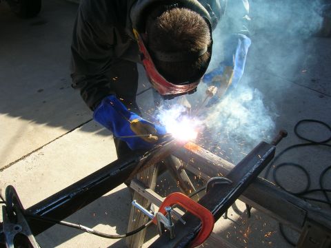 1979 Ford Bronco - A person welds metal components, creating sparks and smoke. The registry claims this is a 1979 Ford Bronco front suspension part.