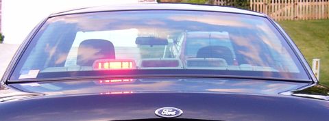 2003 Ford Crown Victoria - The rear of a Ford Crown Victoria is visible, with a light bar inside and another vehicle reflected in the window.