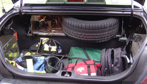 2003 Ford Crown Victoria - The trunk of a 2003 Ford Crown Victoria contains emergency equipment including a spare tire, helmet, and medical bag.