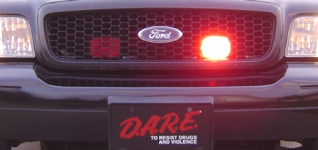 2003 Ford Crown Victoria - Front view of a 2003 Ford Crown Victoria, the Ford emblem, a red emergency light, and a D.A.R.E. license plate.