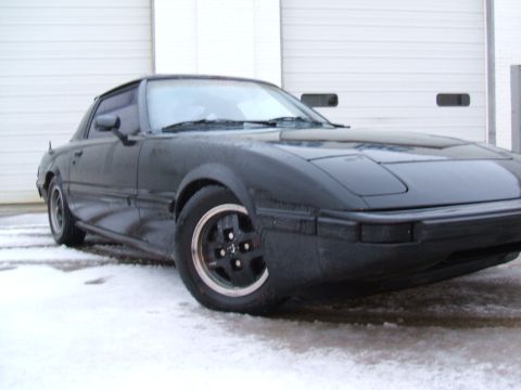 1983 Mazda RX-7 - A black 1983 Mazda RX-7 is shown in a three-quarter front view, parked on a snowy surface.