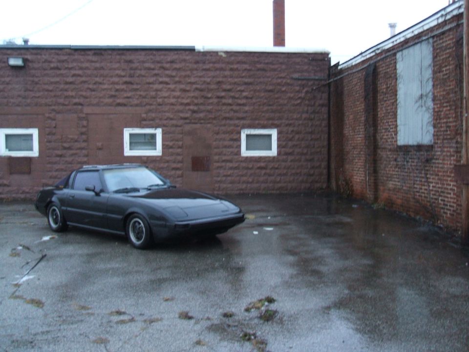 1983 Mazda RX-7 coupe parked in a wet, urban area