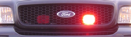 2003 Ford Crown Victoria - Close-up of a Ford grille a prominent Ford emblem and illuminated red emergency lights.