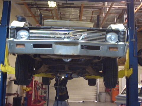 1969 Chevrolet Nova - A mechanic works on the underside of a car elevated on a lift in a garage.