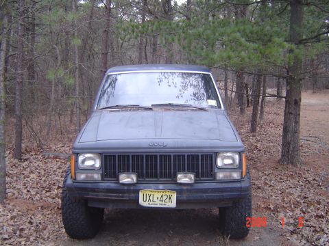 1988 Jeep Comanche - Front view of a 1988 Jeep Comanche pickup truck parked outdoors among trees.