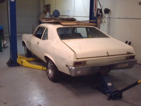 1969 Chevrolet Nova - A white coupe is raised on a car lift, showing its rear end and the underside.