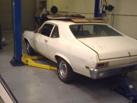 1969 Chevrolet Nova - A white coupe sits on a car lift in a garage, with cardboard stacked on its roof.