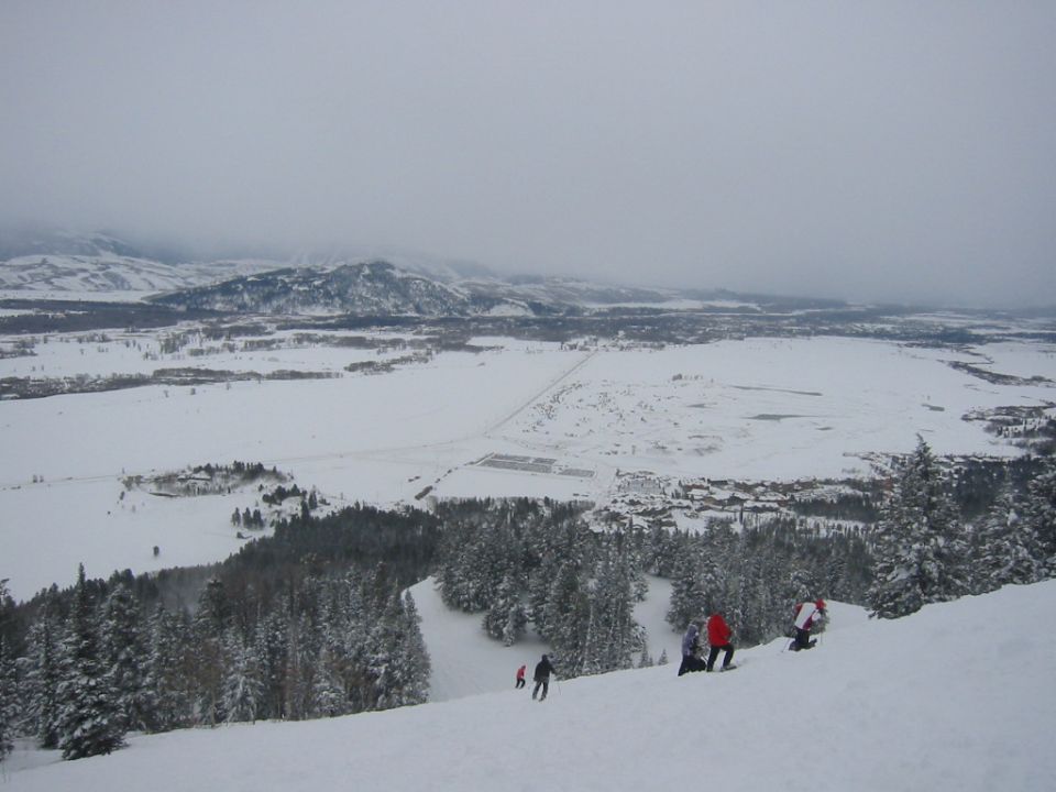 Snowy mountain landscape with skiers on a slope and a distant town