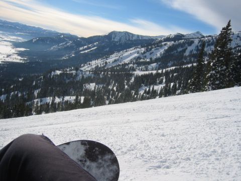 2006 BMW 5 Series - A snowboarder rests on a snowy slope overlooking a vast mountain range and pine forest.
