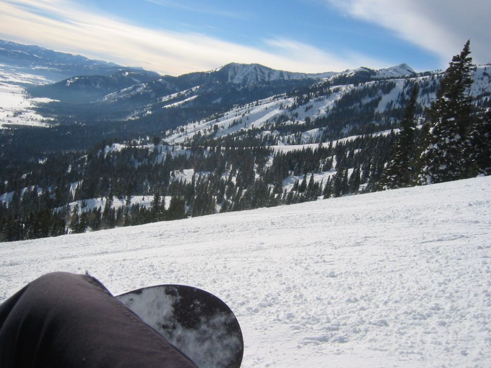 Snowy mountain landscape with snowboarder's leg and snowboard in foreground