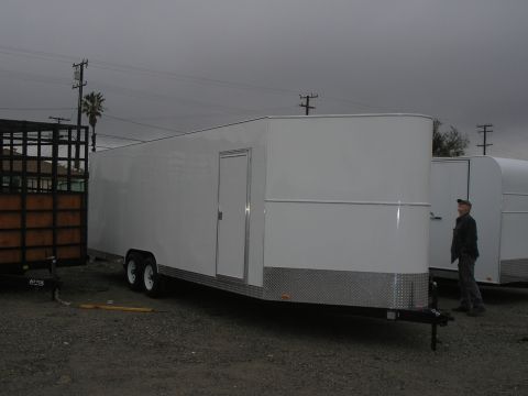 1990 Ford Bronco - Two trailers are parked outdoors under an overcast sky, one is white and enclosed, the other has a black metal cage.