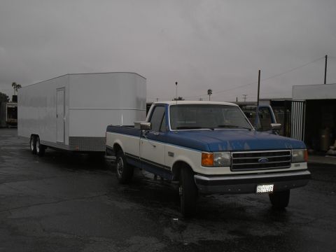 1990 Ford Bronco - A blue and white pickup truck tows a white trailer on a cloudy day.