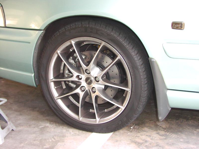 Gunmetal multi-spoke alloy wheel with yellow caliper on light green Volvo sedan, Kumho tire.