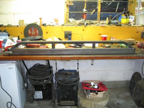 1990 Ford Bronco - Custom fabricated rock sliders sit on a workbench in a garage, ready for installation.