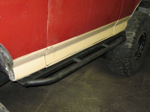 1990 Ford Bronco - Close-up of aftermarket rock sliders installed on the side of a red vehicle with a beige trim line.