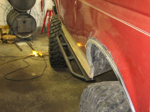 1990 Ford Bronco - Aftermarket rock sliders are visible on the side of a red vehicle with large off-road tires.