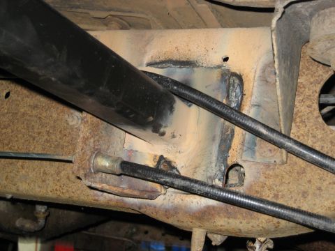 1990 Ford Bronco - Close-up view of rock sliders mounted to a rusty vehicle frame, with black cables visible.