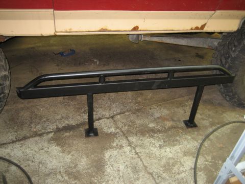1990 Ford Bronco - Aftermarket rock sliders are attached to the frame of a vehicle, with the tires visible on either side.