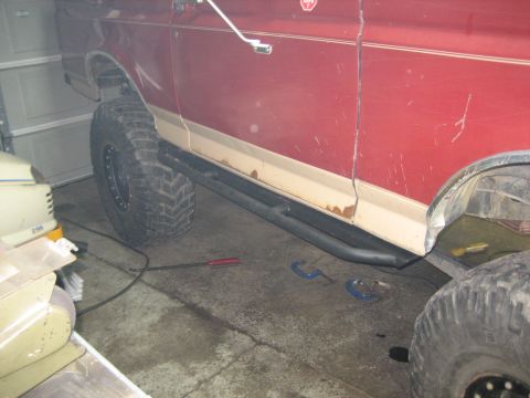 1990 Ford Bronco - This red SUV, likely a 1990 Ford Bronco, is equipped with aftermarket rock sliders and large off-road tires.