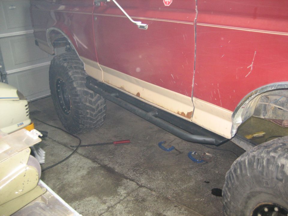 Red SUV side view showing large tires and black rock sliders. Some rust is visible on the lower body trim