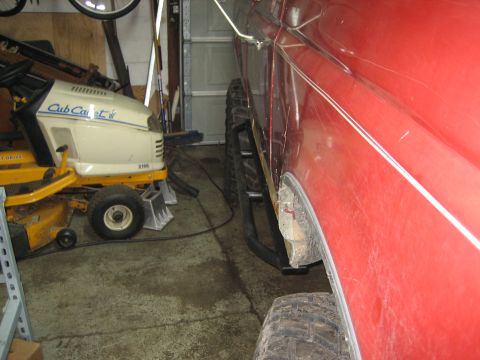 1990 Ford Bronco - Side view of a red SUV with aftermarket rock sliders and visible rust on the fender.
