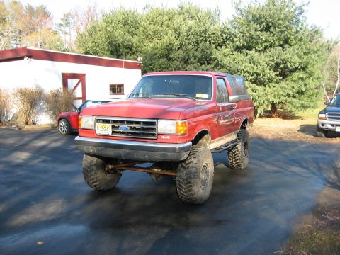 1990 Ford Bronco - This red Ford Bronco features a lifted suspension and oversized tires, suggesting off-road modifications.