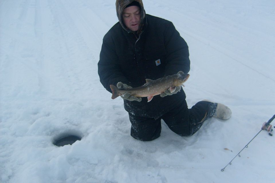 Man holding a fish on ice with a fishing rod nearby