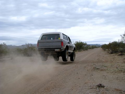 1980 Ford Bronco - This vehicle is airborne on a dusty dirt road in a desert landscape.
