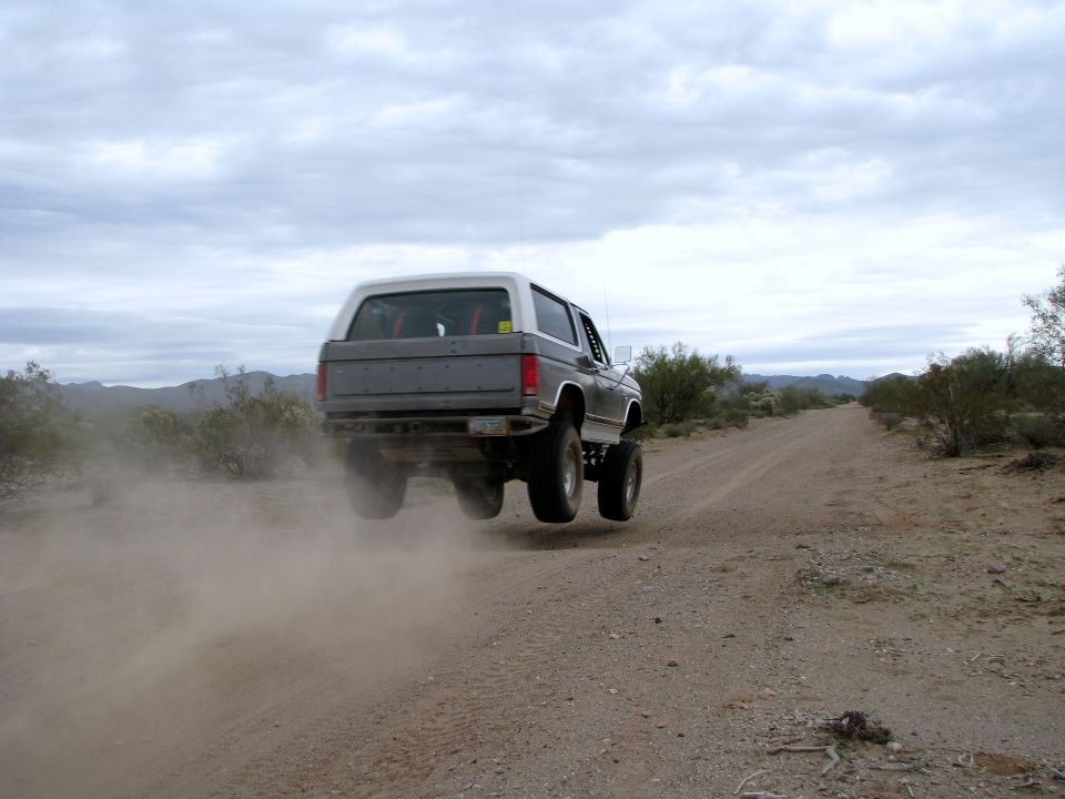 Bronco airborne on dirt road, kicking up dust. White top, grey body