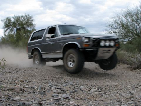 1980 Ford Bronco - This Ford Bronco is navigating a dusty, off-road path with a modified front bumper and auxiliary lights.