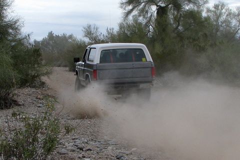 1980 Ford Bronco - A 1980 Ford Bronco drives off-road, kicking up a cloud of dust.