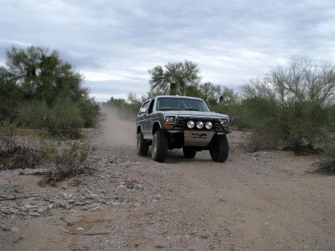 1980 Ford Bronco - This modified Ford Bronco is navigating a dusty desert trail under an overcast sky.