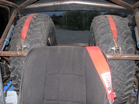 1980 Ford Bronco - The interior of a modified vehicle shows two large spare tires secured with red straps, along with a safety harness.