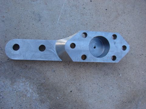 1979 Ford Bronco - A custom metal part with a machined cylindrical recess and several bolt holes is shown against a concrete surface.