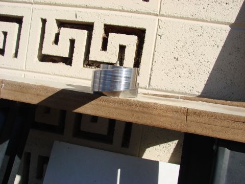1979 Ford Bronco - An aluminum component with a ribbed surface is placed on a wooden plank in front of a patterned block wall.
