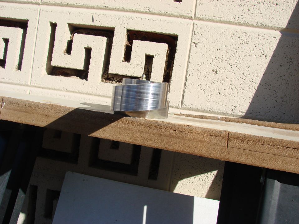 Aluminum part with ribbed texture sits on a wooden surface against a decorative block wall