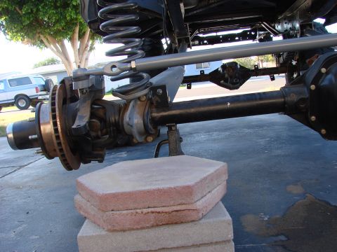 1979 Ford Bronco - Close-up view of vehicle front suspension and axle components, with a blue SUV visible in the background.