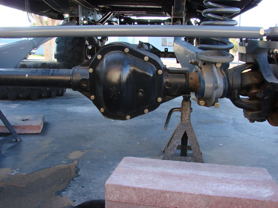Rear axle assembly with differential cover, supported by jack stands. A large gray bar runs above the axle