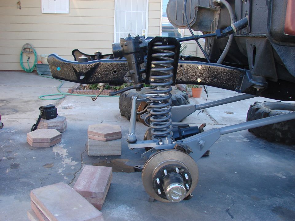 Vehicle front suspension assembly with coil spring and brake rotor visible. Frame section is black