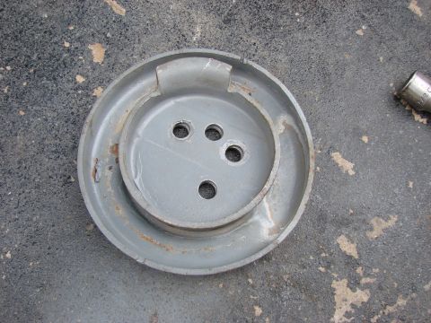 1979 Ford Bronco - A gray metal hubcap with four bolt holes lies on an asphalt surface, possibly awaiting installation or removal.