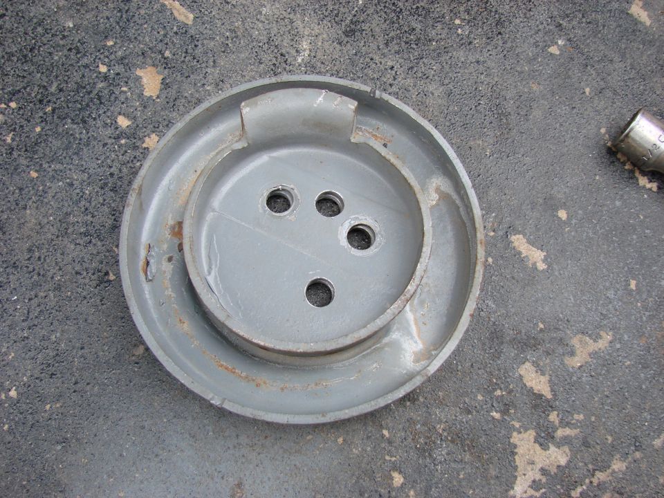Gray metal hubcap with four bolt holes on asphalt