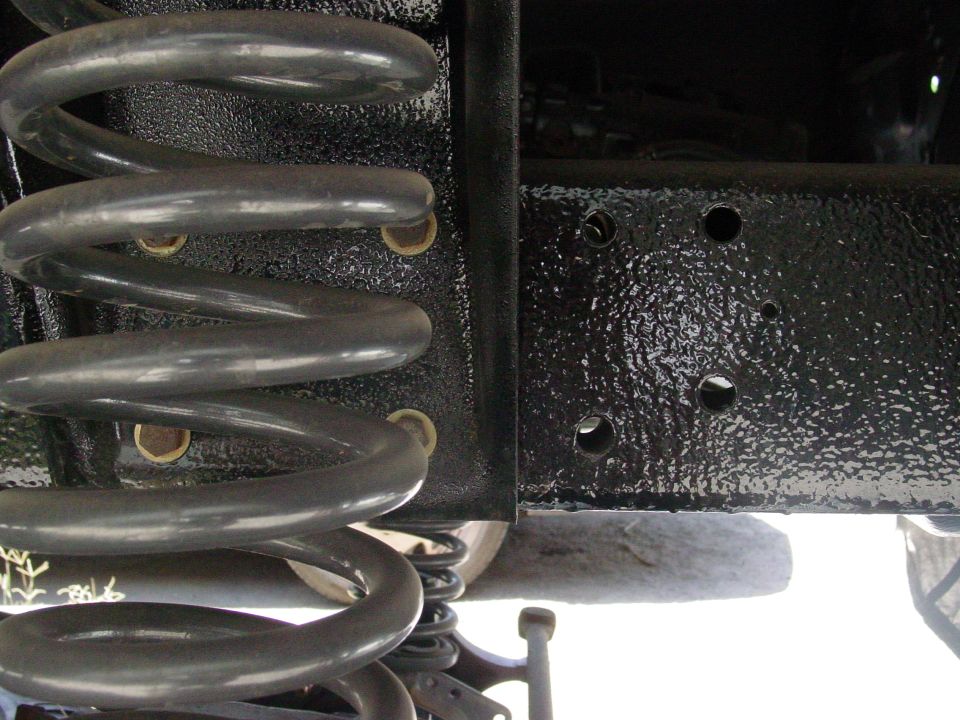 Close-up of a large coil spring and black painted frame section of a vehicle