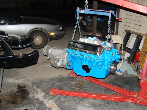 1979 Ford Bronco - A V8 engine and transmission assembly, painted bright blue, is suspended by an engine hoist, likely for installation or removal.