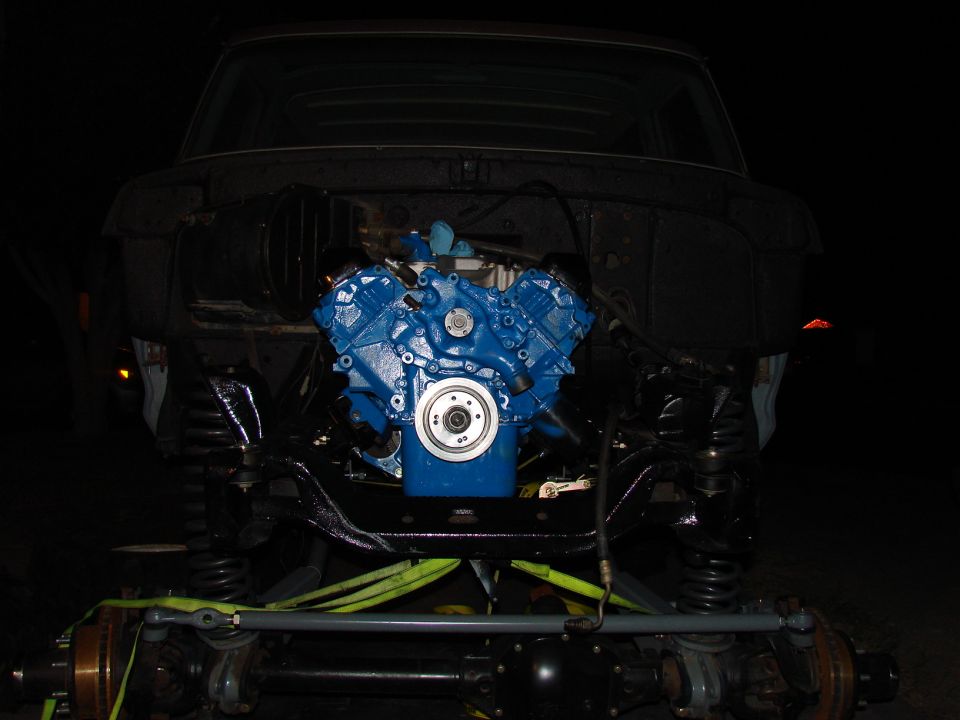 blue engine in a vehicle frame, front end removed, suspension visible