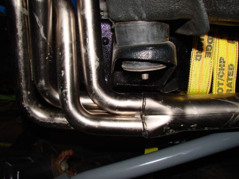 1979 Ford Bronco - Close-up view of exhaust headers and a vehicle's engine mount, with yellow straps visible.